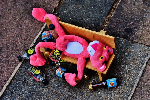 pink panther stuffed animal on bench surrounded by beer bottles