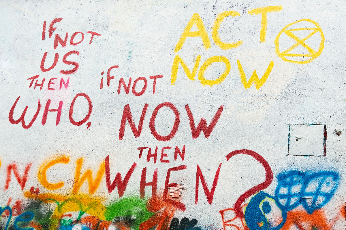 A white wall with graffiti reading Act now, If not us then who? I fnot now then wehn?