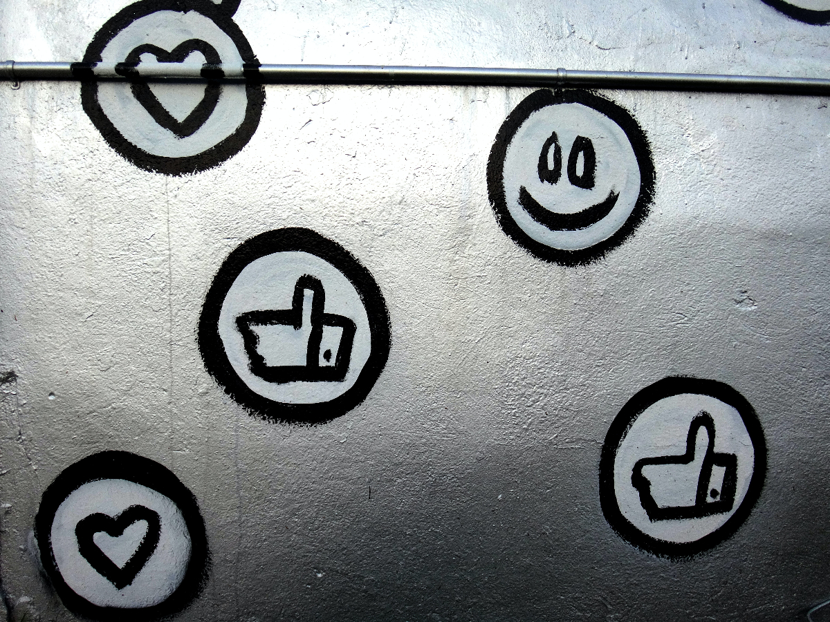 A wall with smiles, hearts and thumbs up, likes painted on it.