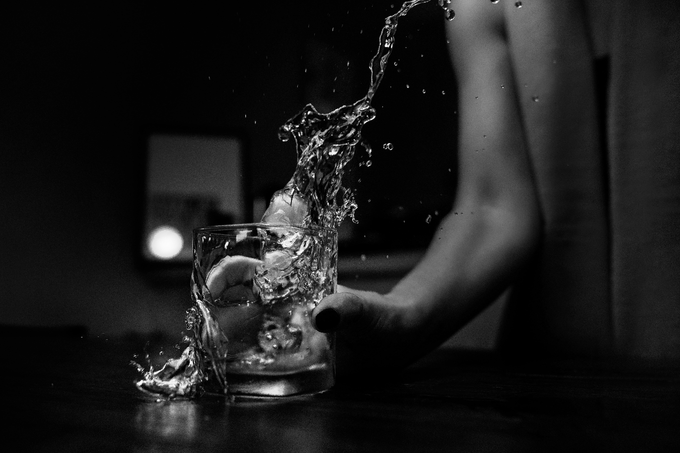 A woman pouring a glass of whiskey and missing the glass
