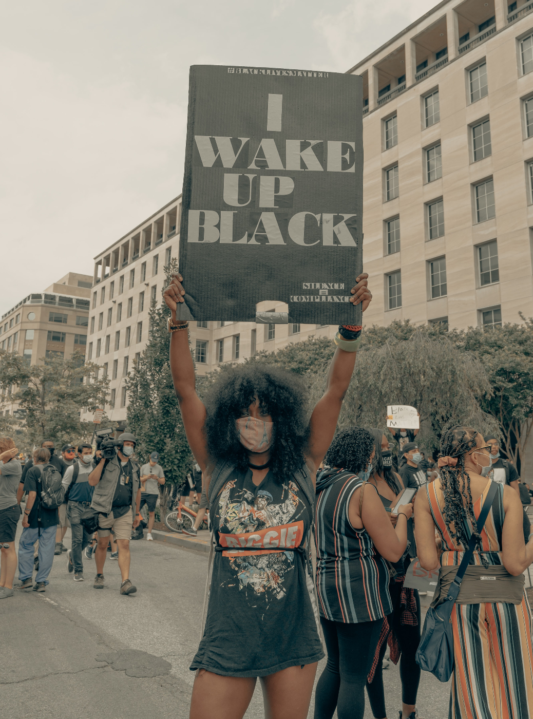 A young black woman at a protest holdning a sign t at reads, I Wake Up Black
