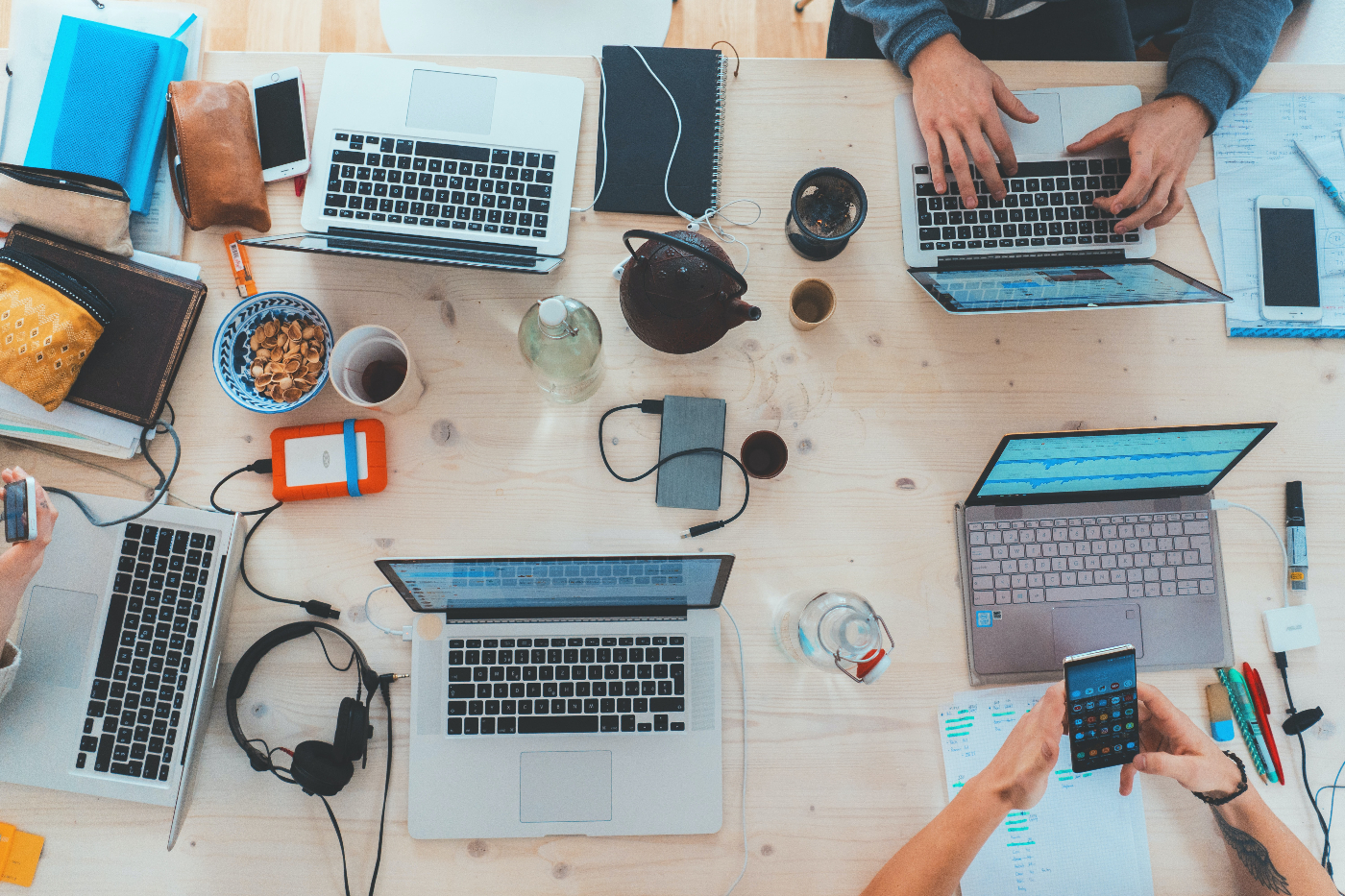 A table full of lapstops, coffee mugs, tea cups, headphones and writing instruments