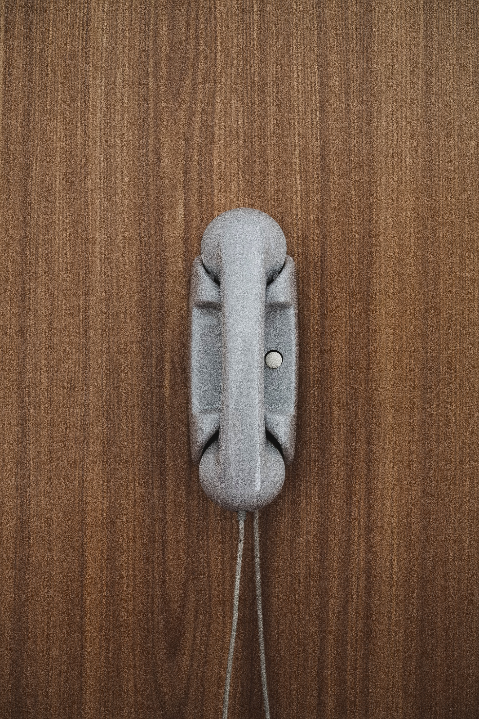 a gray phone with one button hanging on a wood panel wall
