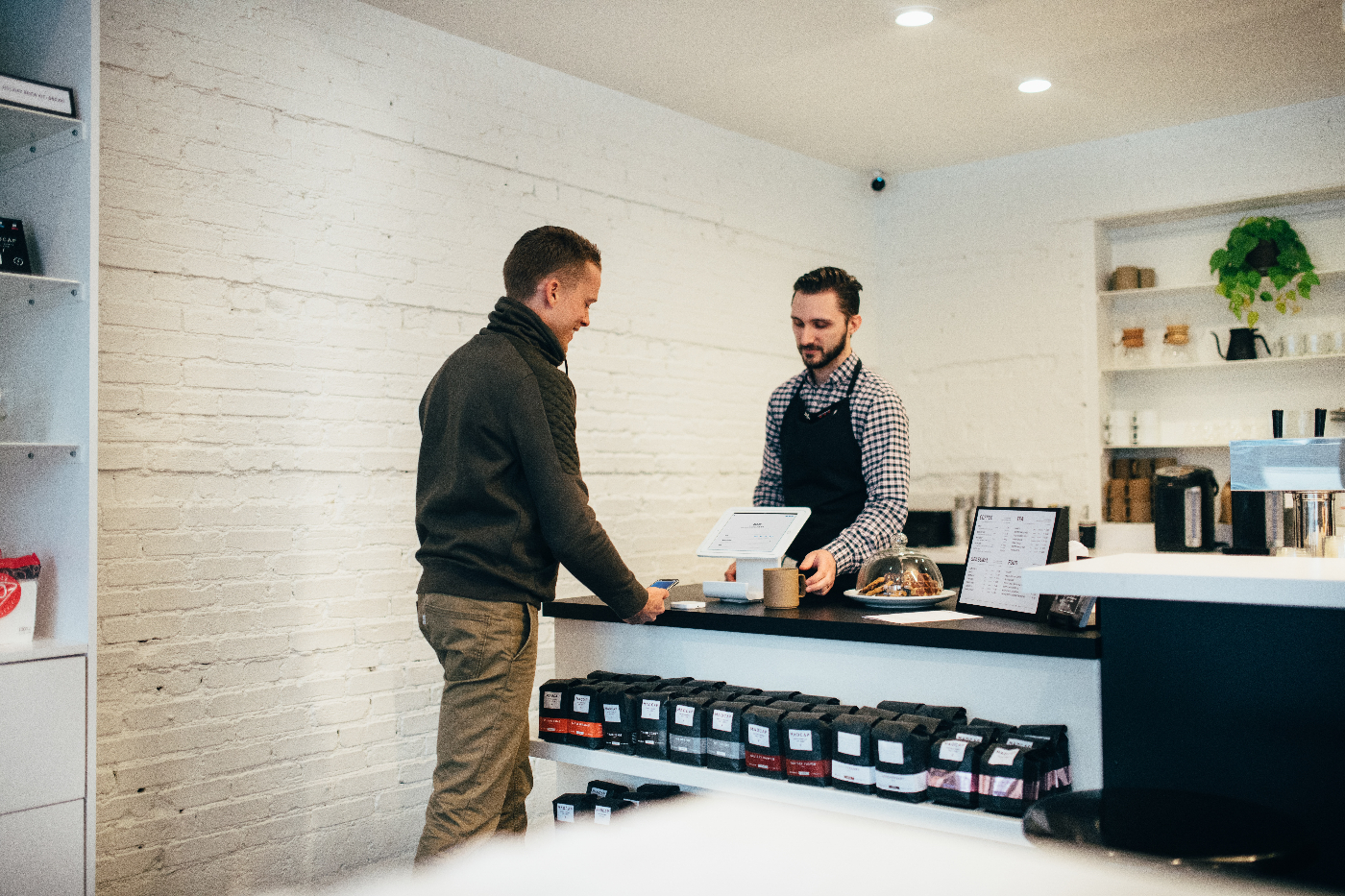 A customer and a clerk in a coffee shop, customer is using PoS technology