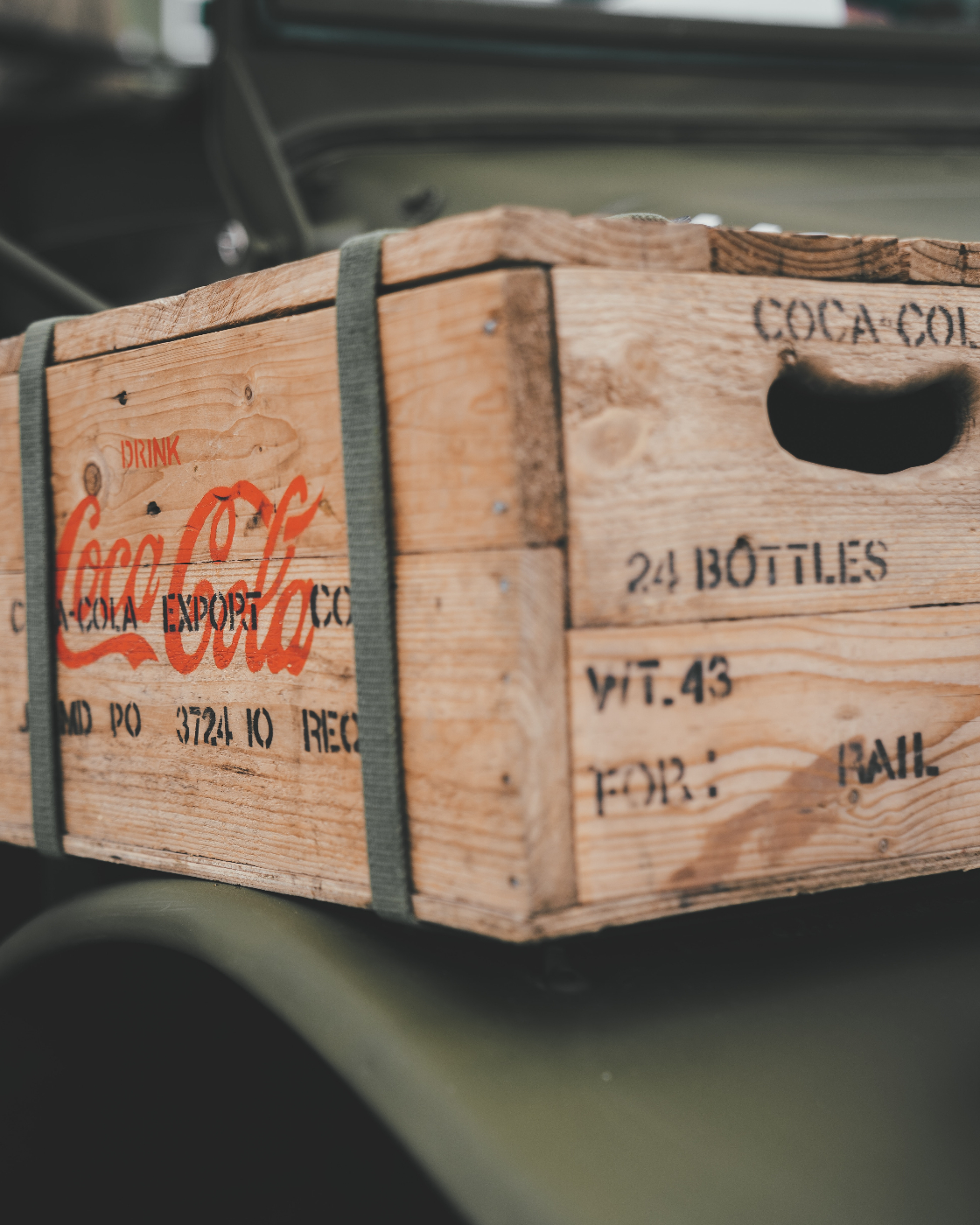 An antique wood case of Coca-Cola, strapped to the fender of an old car