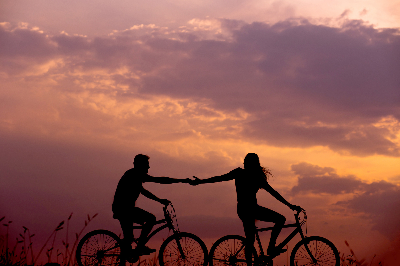 A couple on bikes, the woman reaching back for the hand of the man behind her