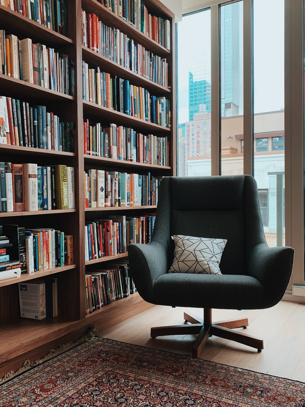 A plush green swivel chair and an area rug beside a floor to ceiling book case