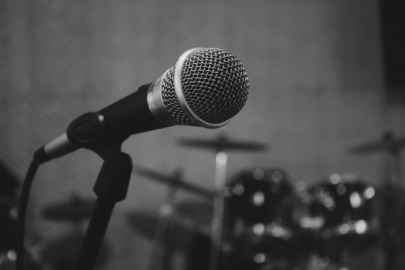 black and white shot of a mic on a stand with a drum kit in the background