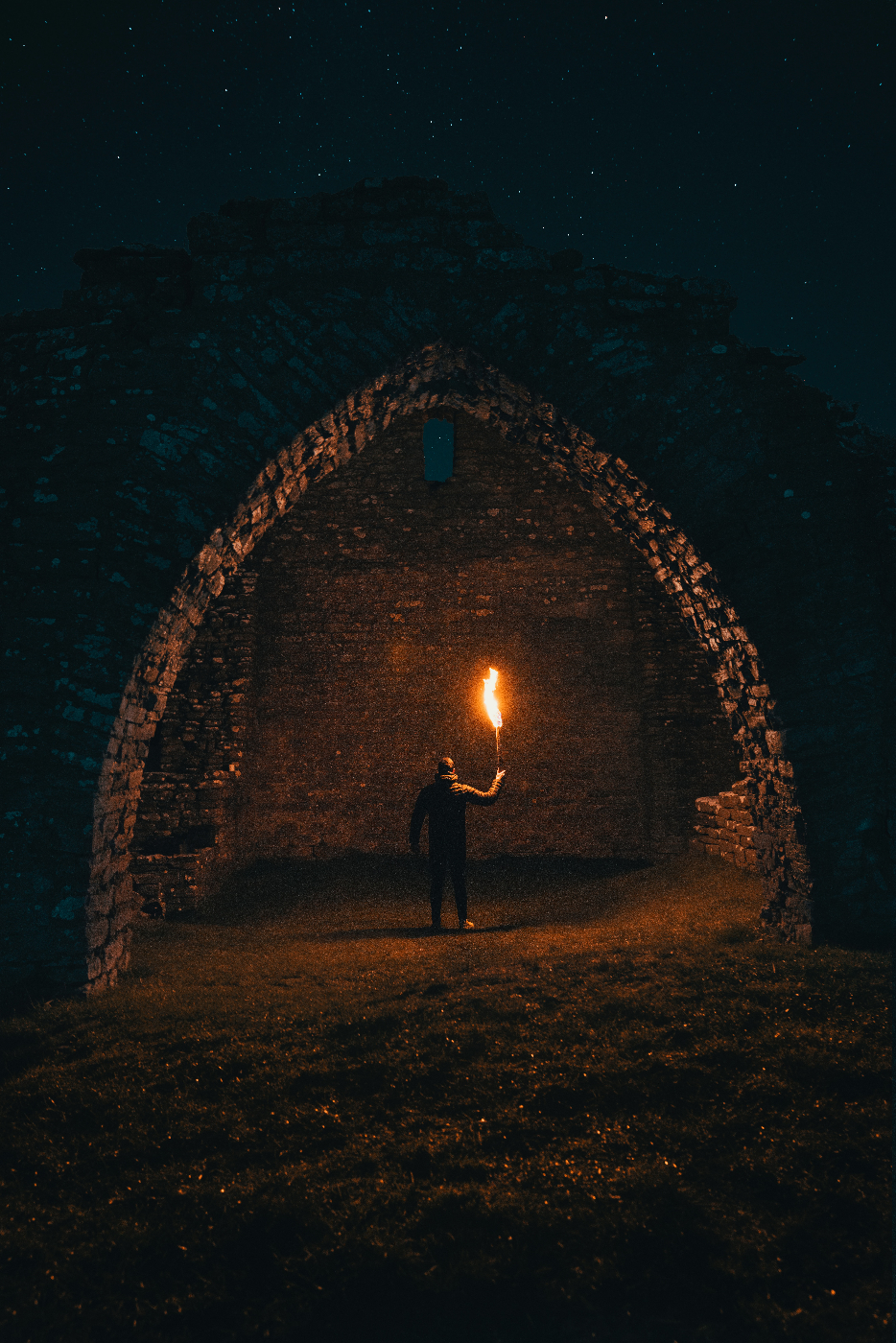 A man with a torch standing beneath an underground stone arch