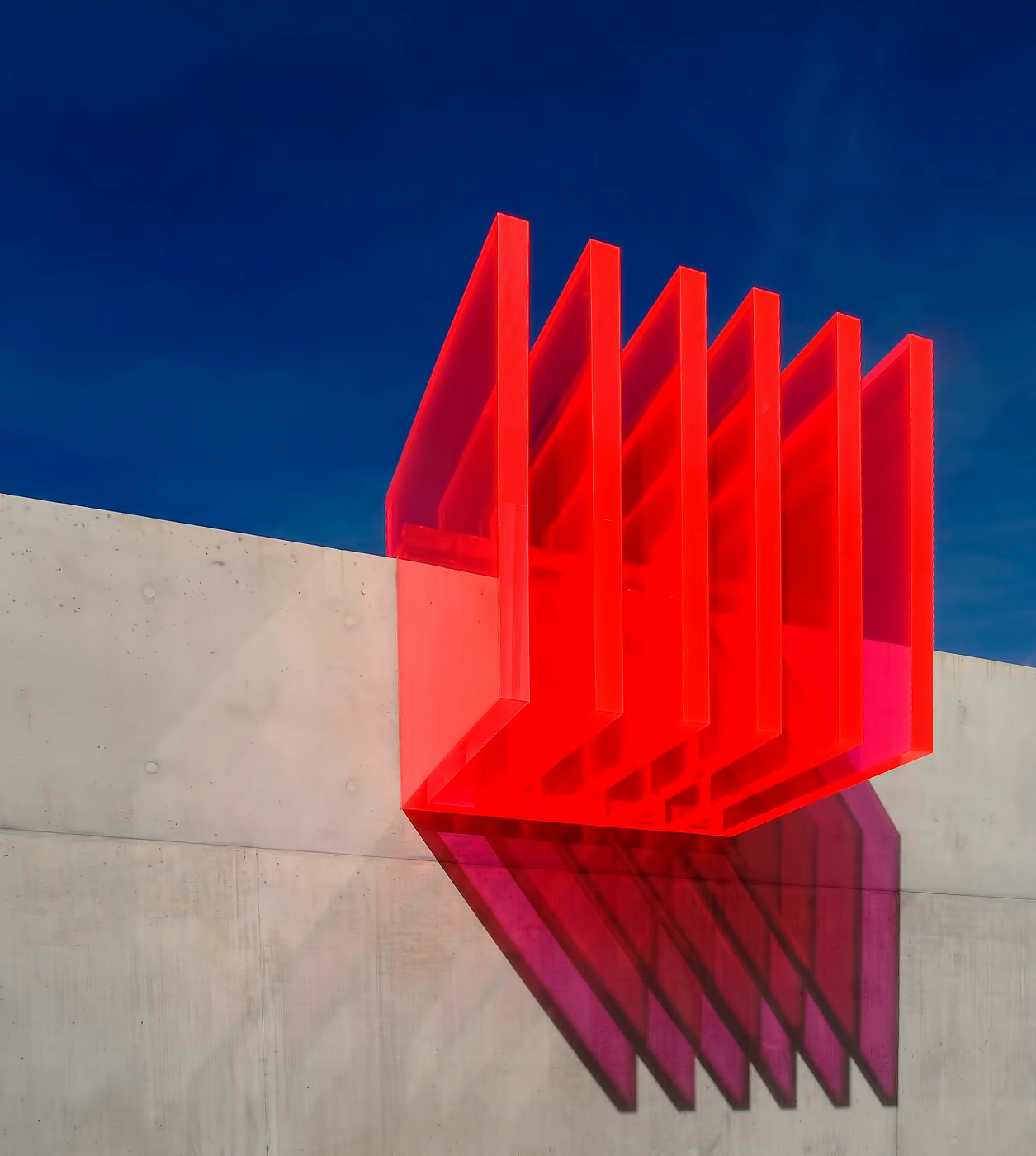 Transparent red panels on the side of a building reflecting pink and purple light on the wall