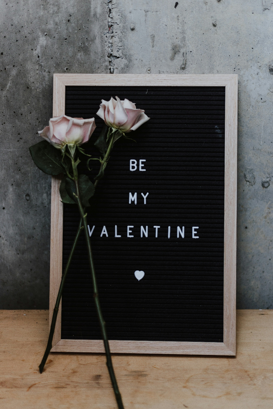 Two pale silver roses propped against a sign reading Be My Valentine and a tiny heart