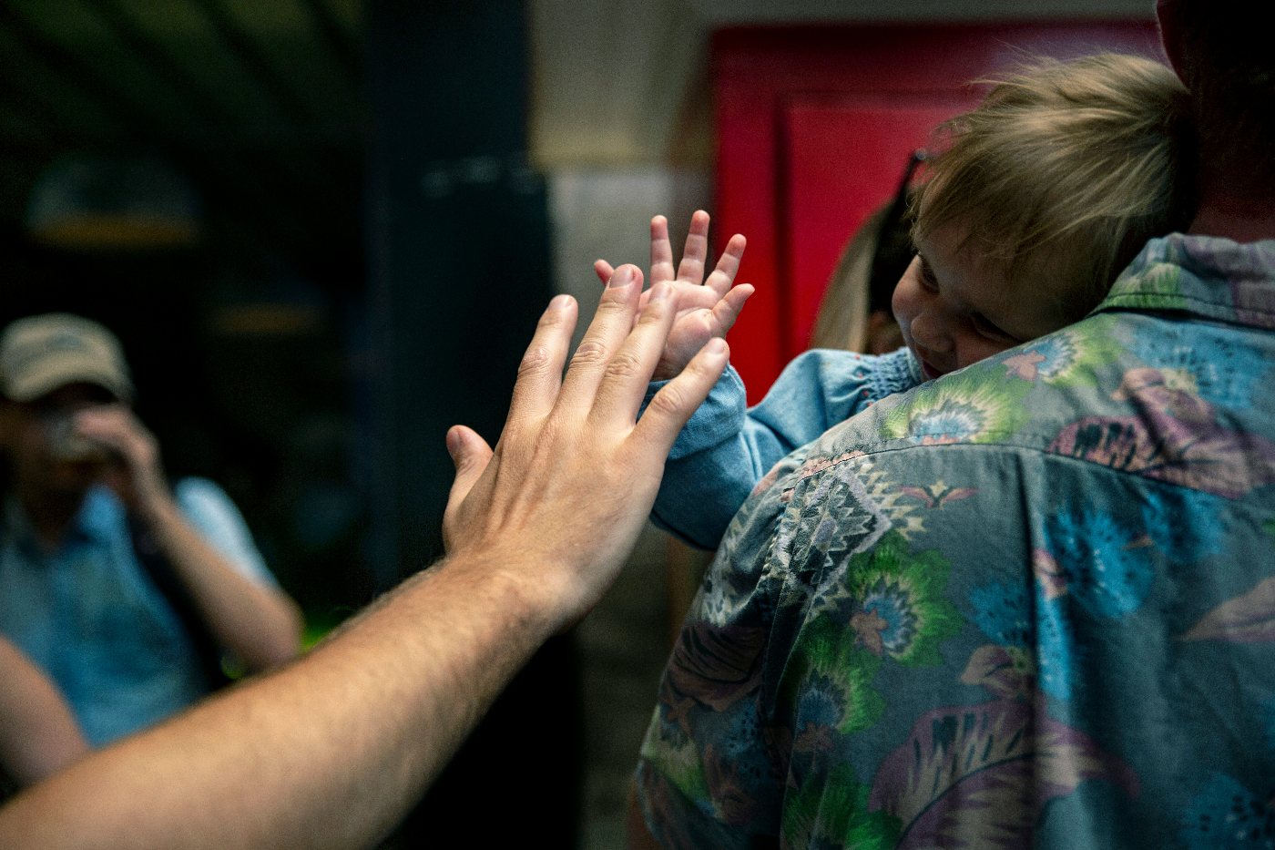 A small child on his parent's  shoulder getting  a high five from another person