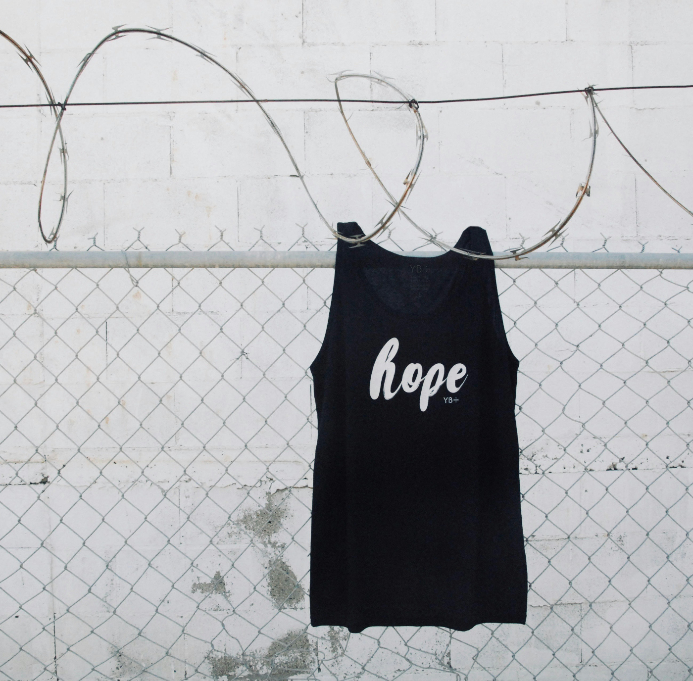 A fence with razor wire on top and a black t-shirt with the word hope hanging on the razor wire
