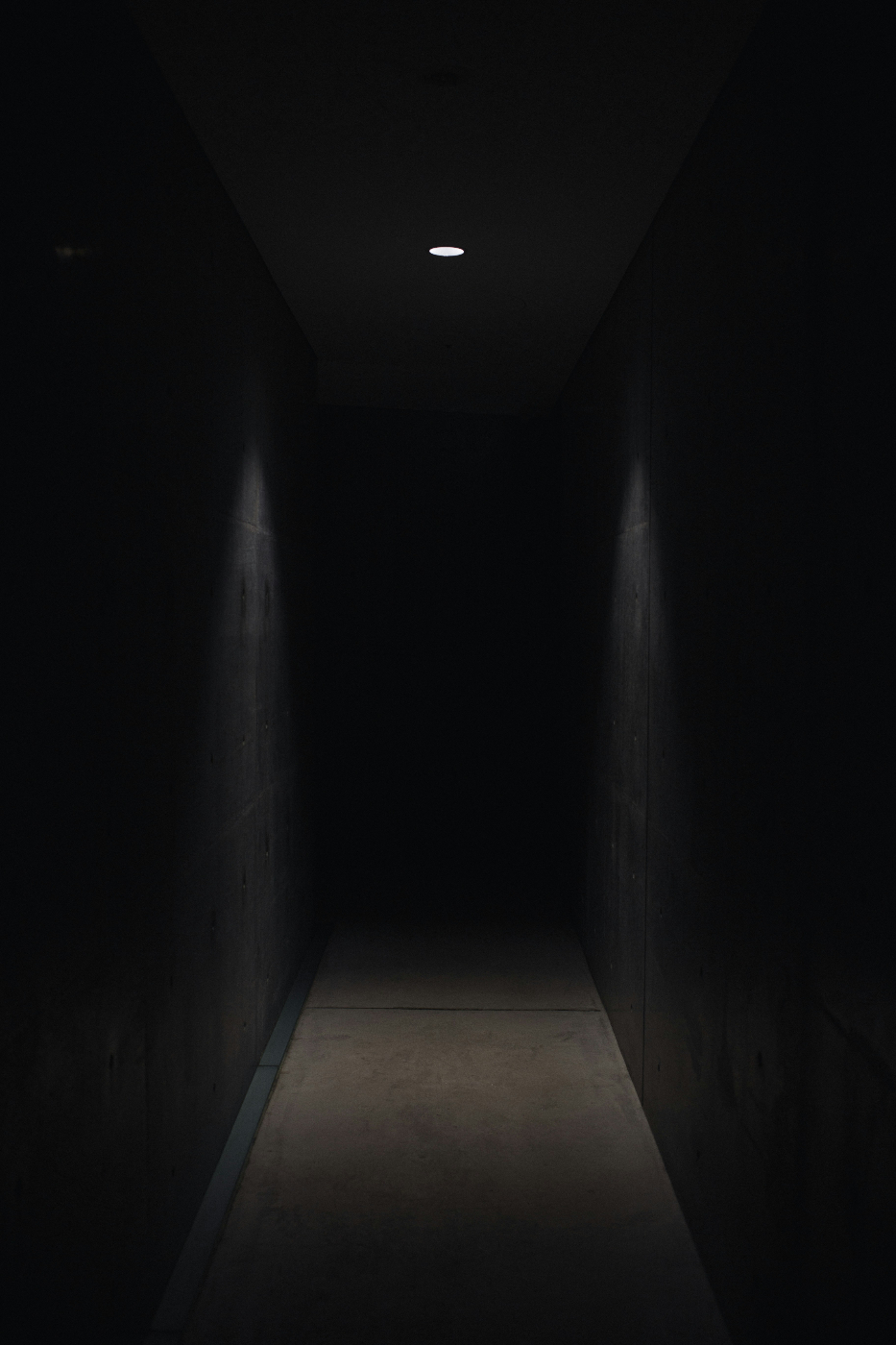 A dark hall with a tiny overhead light casting triangular light on the walls