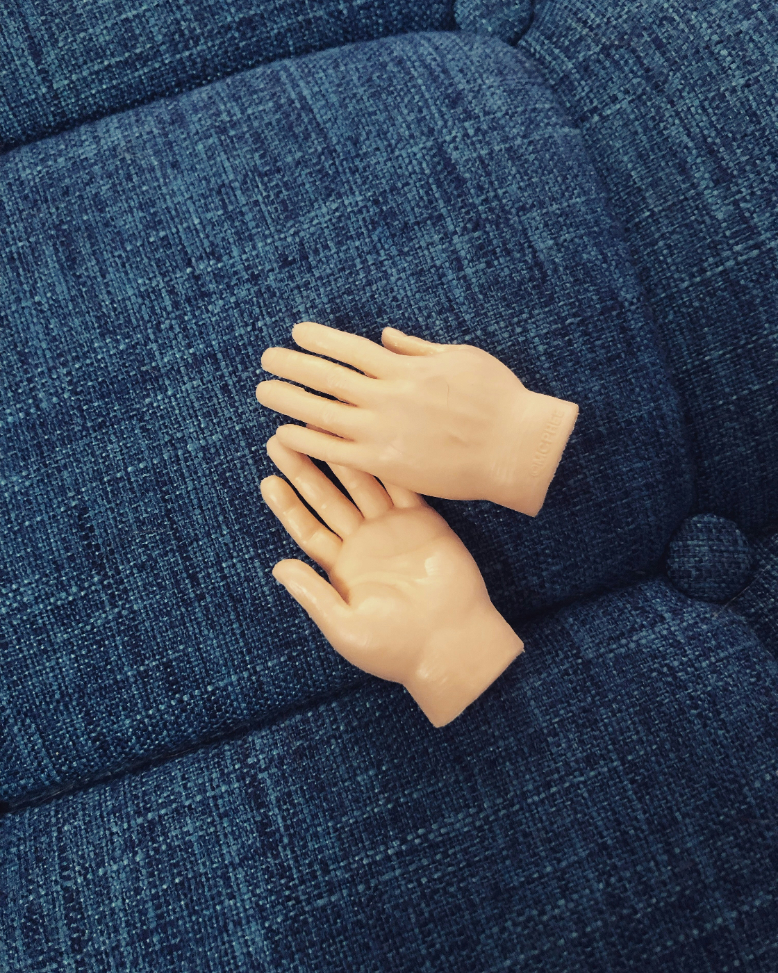 Two fake hands sitting on a blue couch