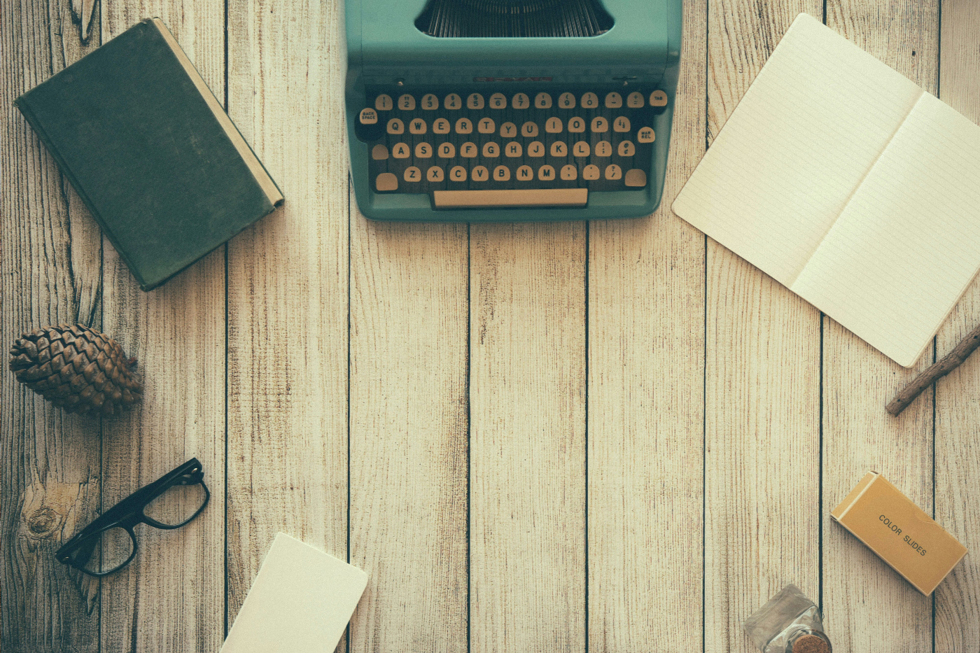A typewriter, blank book, books, glasses pine cone pencil and instruments of inspiration