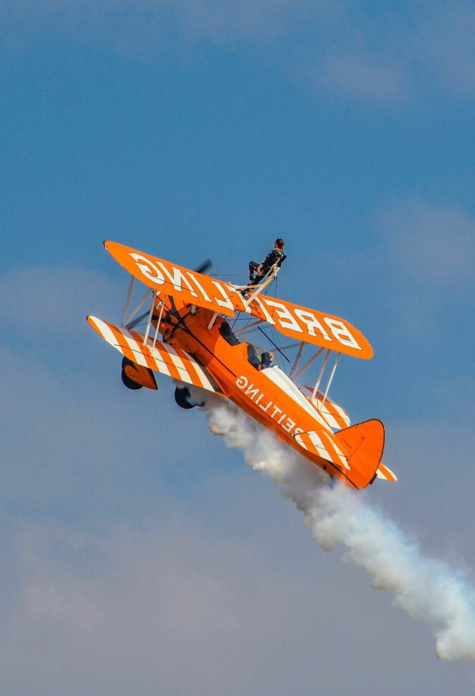 A wing walker on an orange and white bi-plane
