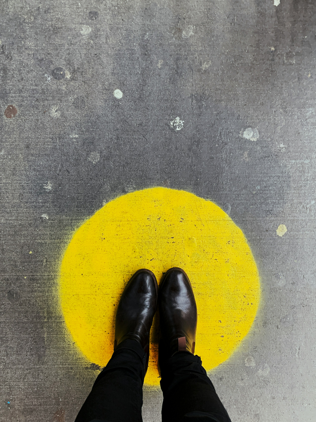 A person in black pants and shoes standing on a yellow circle painted on the ground