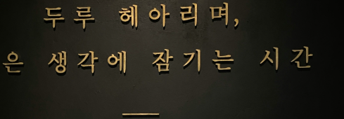 A black wall with gold letters in Korean and English reading: Time to lose yourself in deep wandering thought