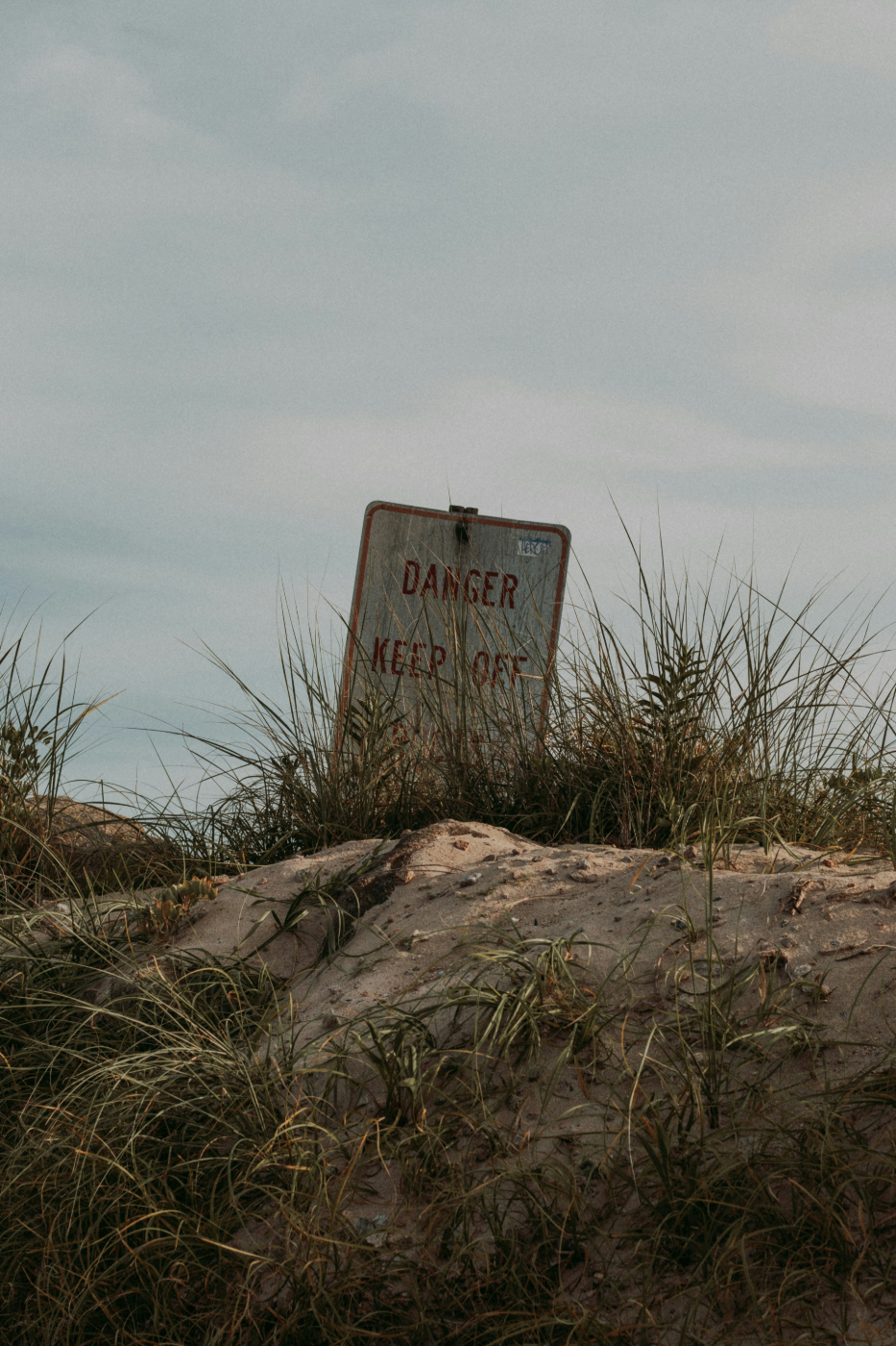 A sand dunes and sand grass partially blocking a danger sign