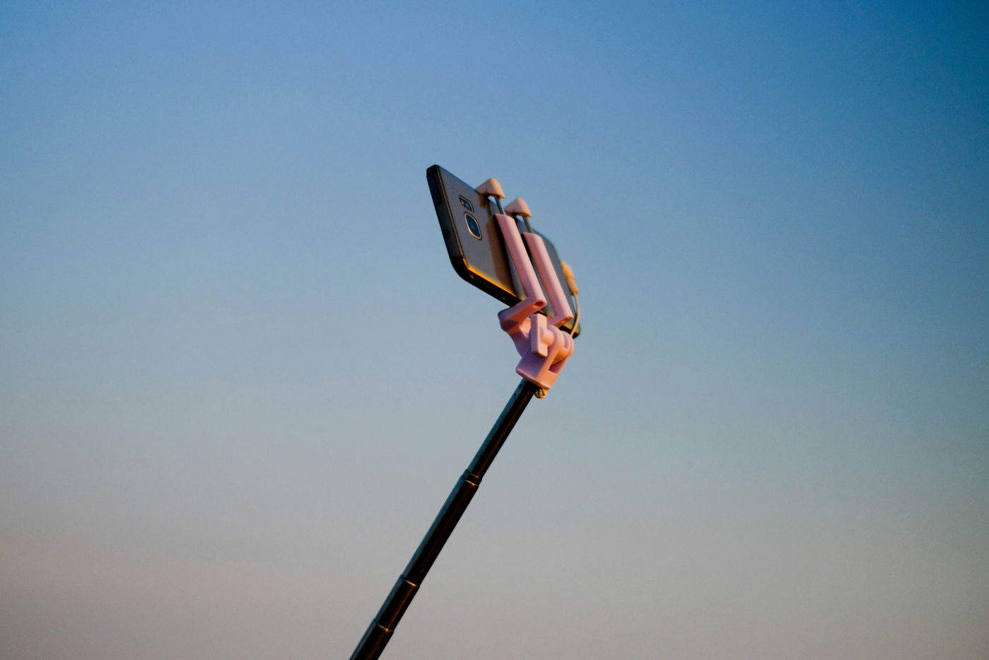 A smartphone on a selfie stick against a blue sky