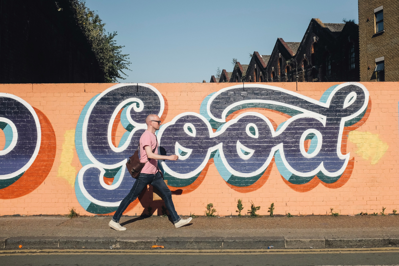 A man walking by an orange wall with the word GOOD painted on it in 3D style