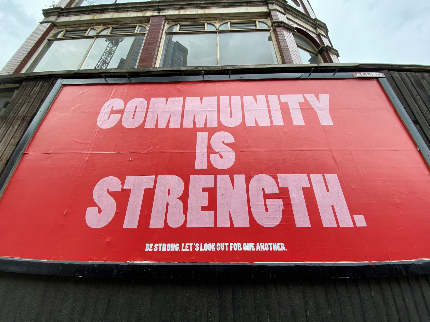 A red sign on the side of building reading Community is Strength: Be strong. Let's look out for one another