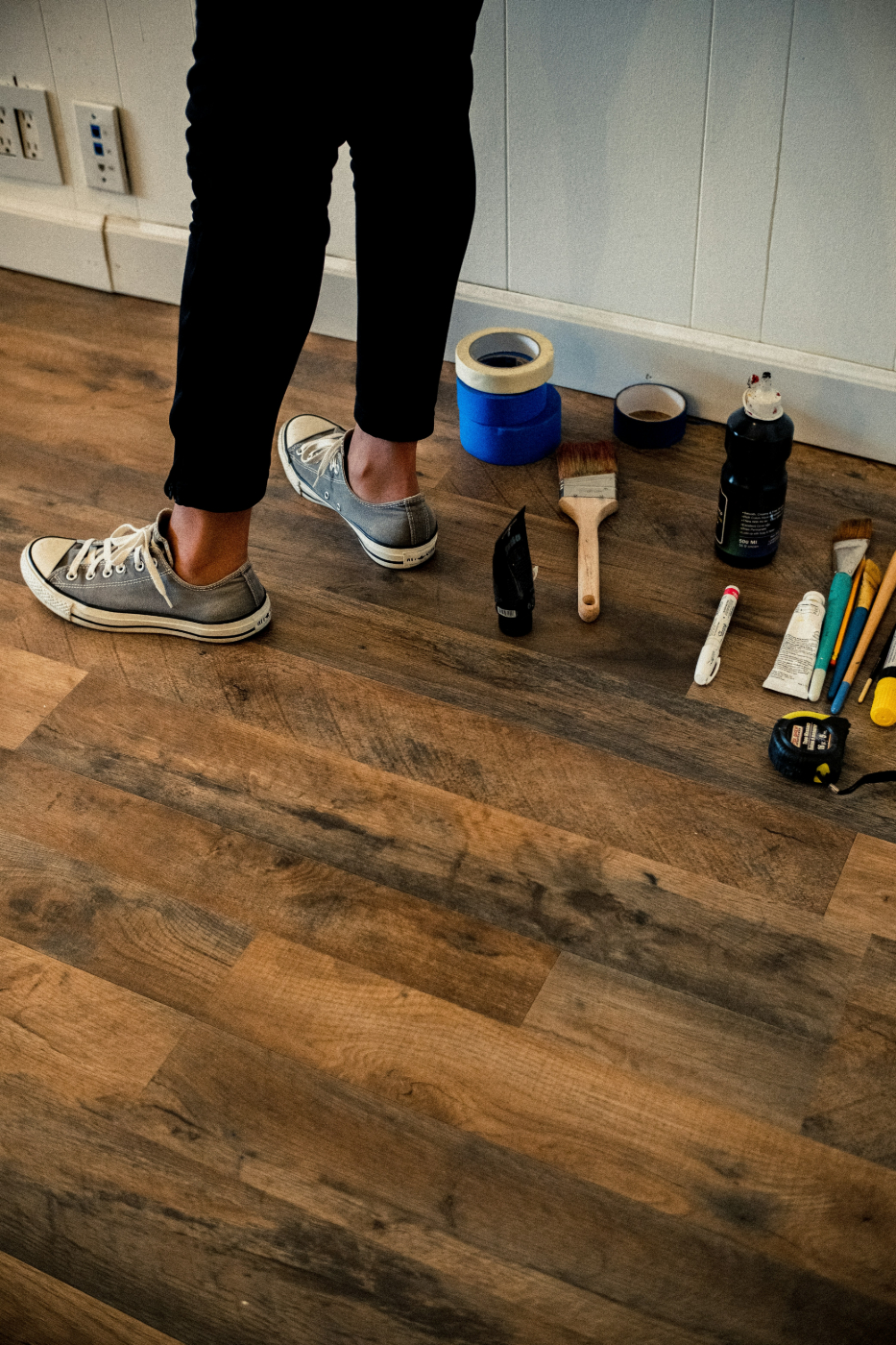 The legs of a person on a wood floor surrounded by tools for a home improvement job