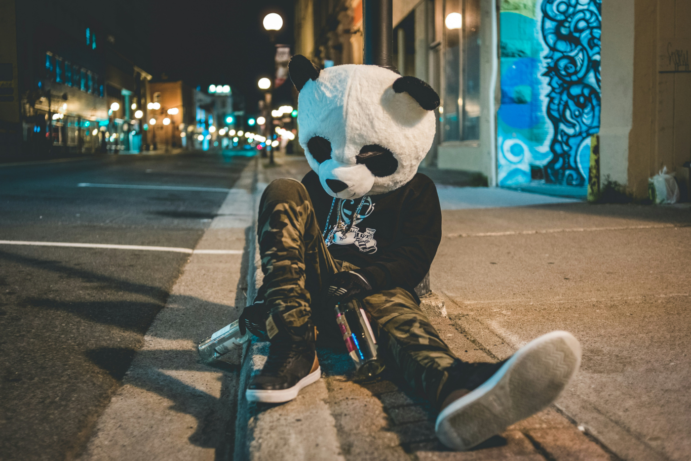  person in camo pants, black T-shirt and a panda head holding two empty bottle of vodka