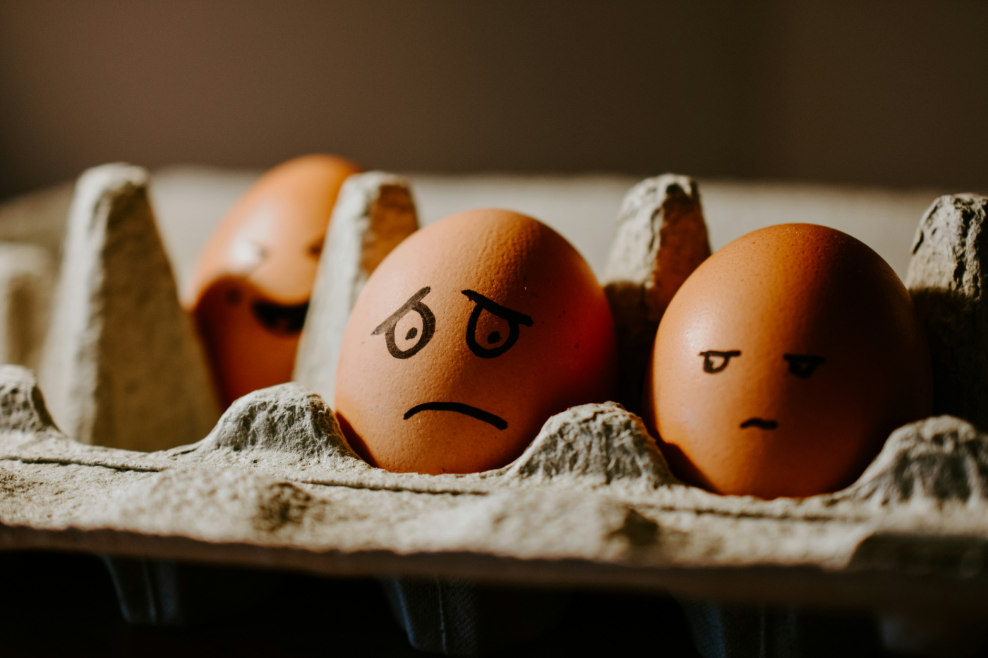 3 brown eggs in a carton with face drawn on. One smiling, one looking worried and one giving side eye