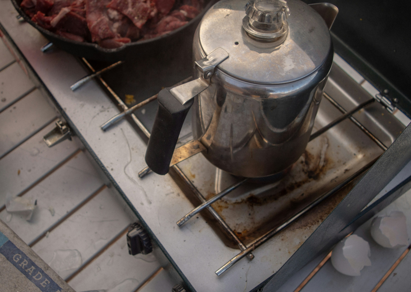 An old, silver percolator on a camp stove