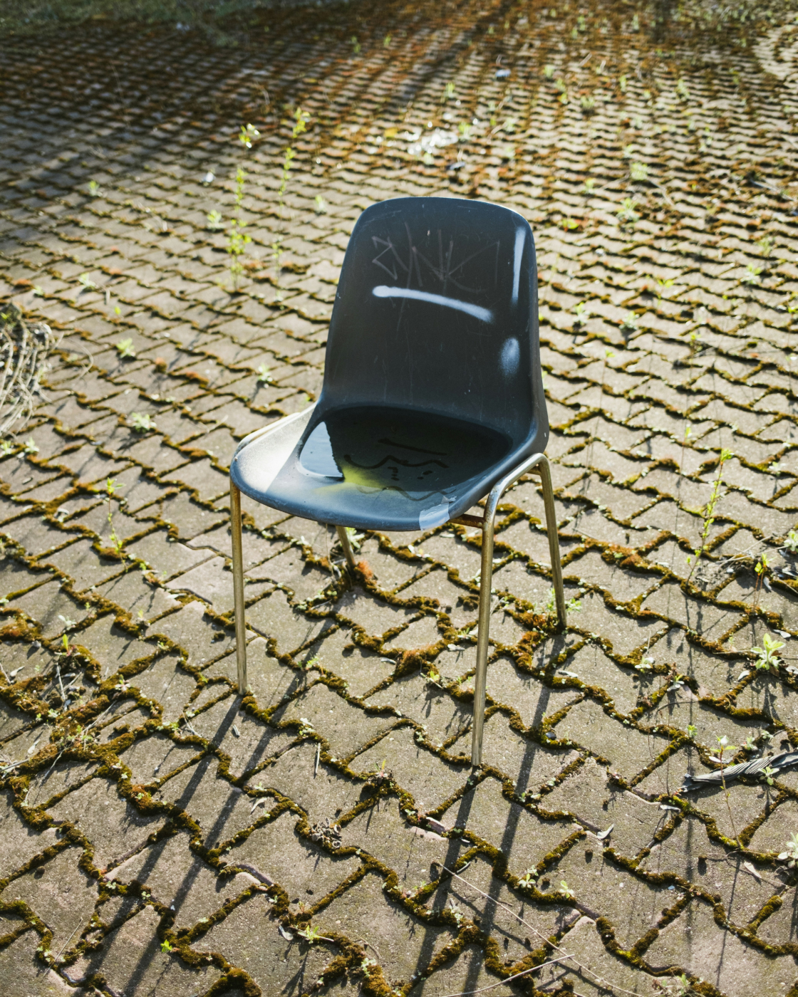A blue plastic chair covered in graffiti sitting on a cobblestone patio