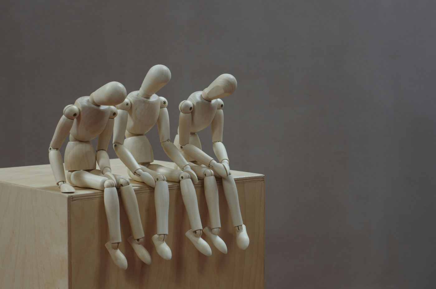 Three manikins, all with heads down, sitting on a block