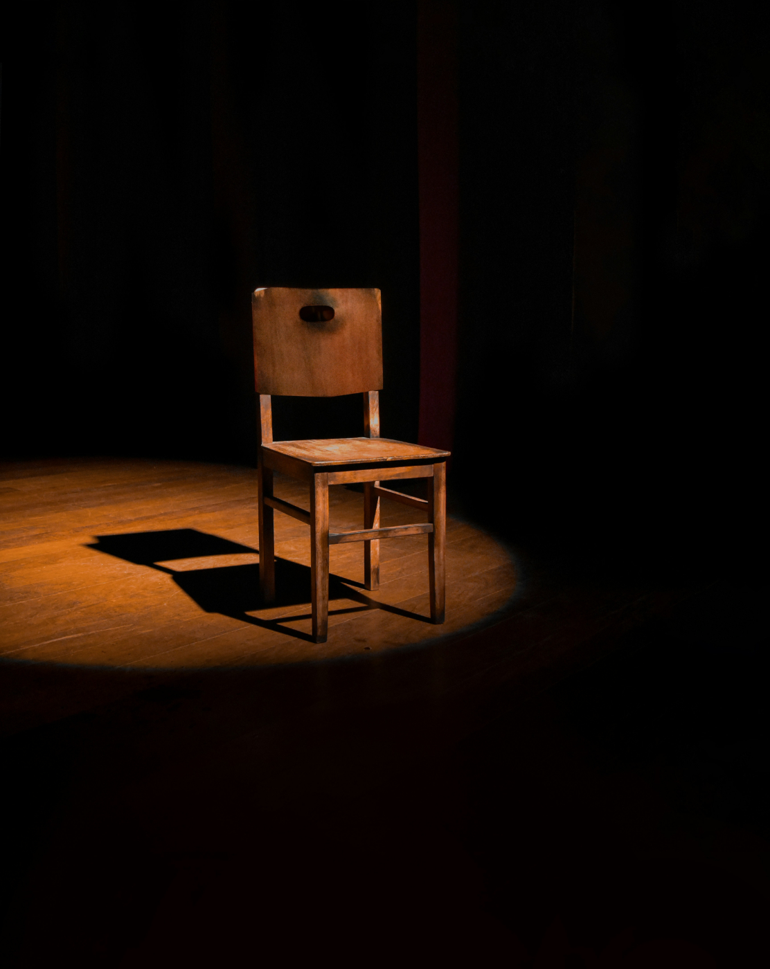 An empty wooden chair in a down light on a stage