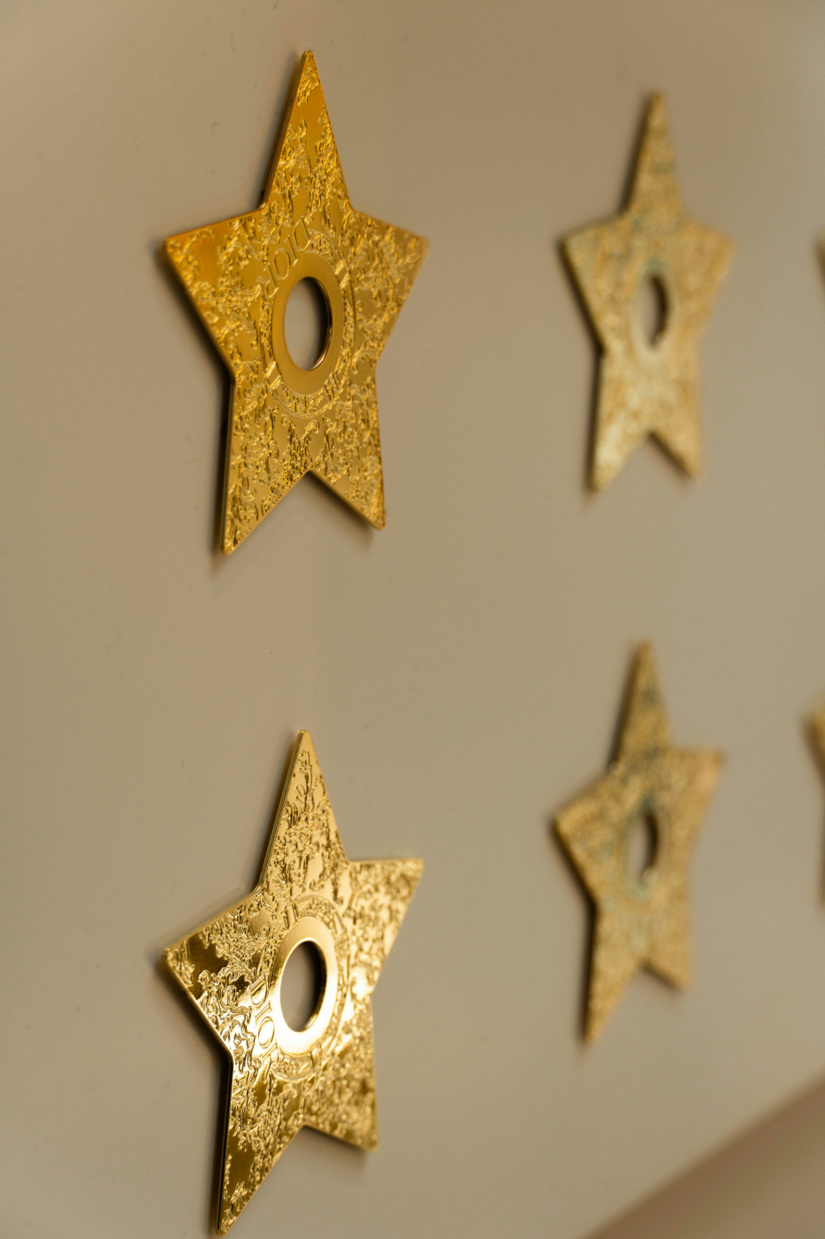 4 gold stars with holes in the middle stuck to a beige wall