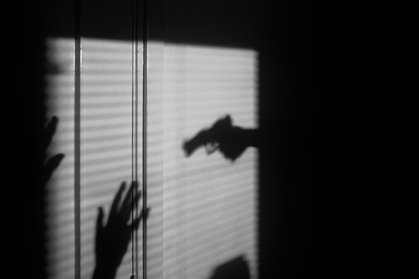 A shadow on a wall of a hand holding a gun pointing it at two upraised hands in surrender