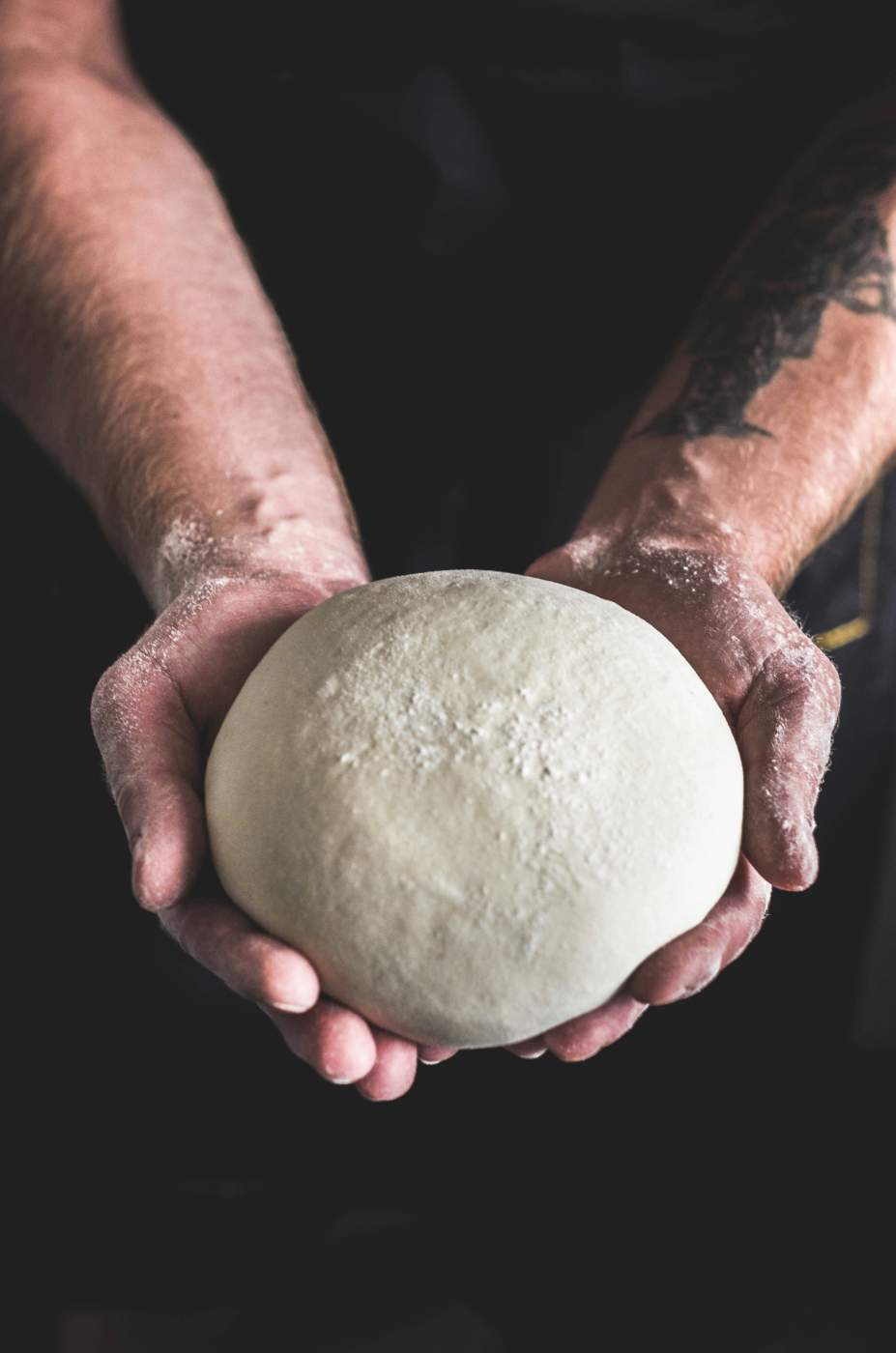 A guy's flour covered hands holding a large ball of pizza dough