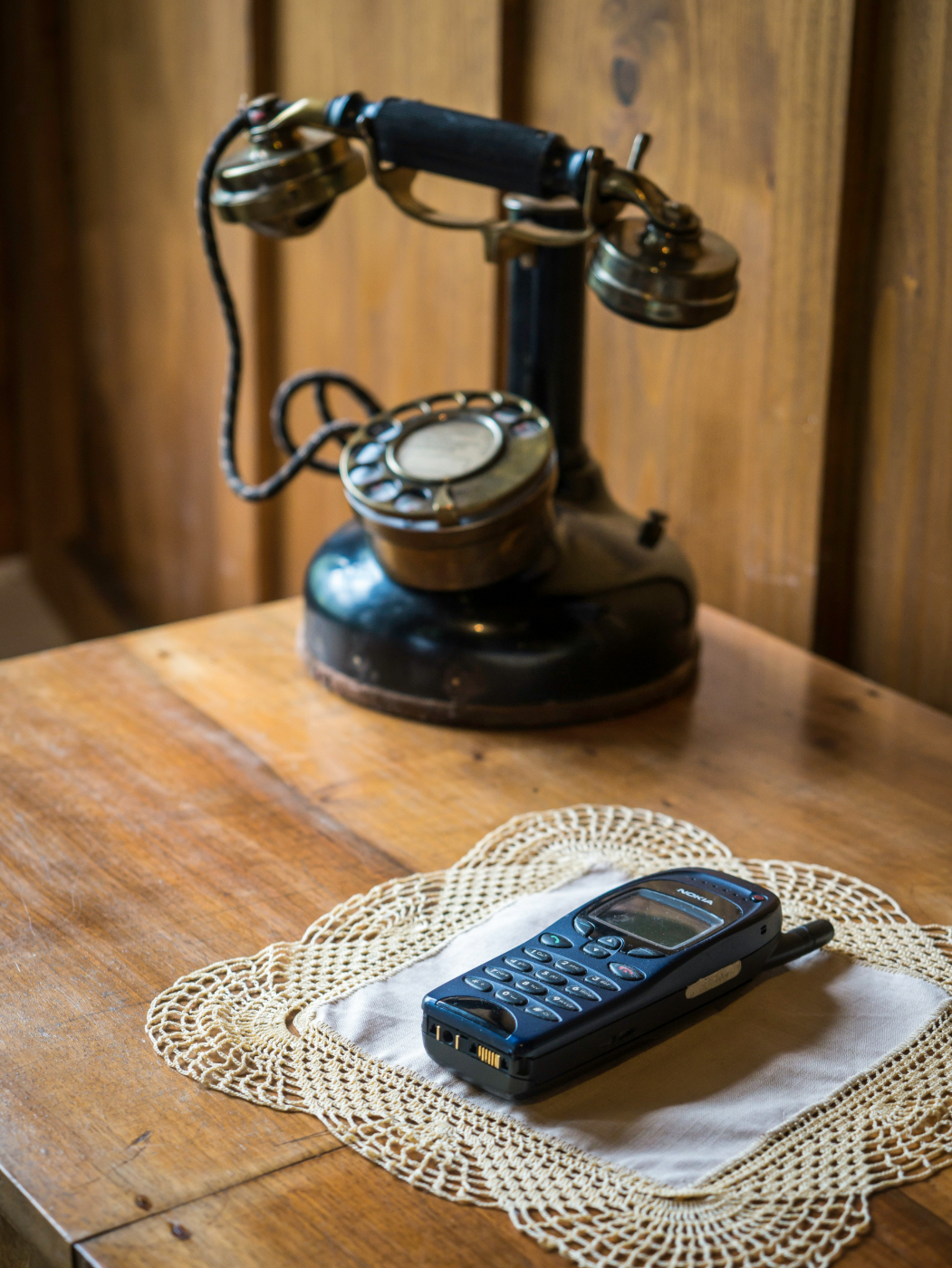 An antique black cradle phone next to a Nokia cell phone sitting on a lace doilie