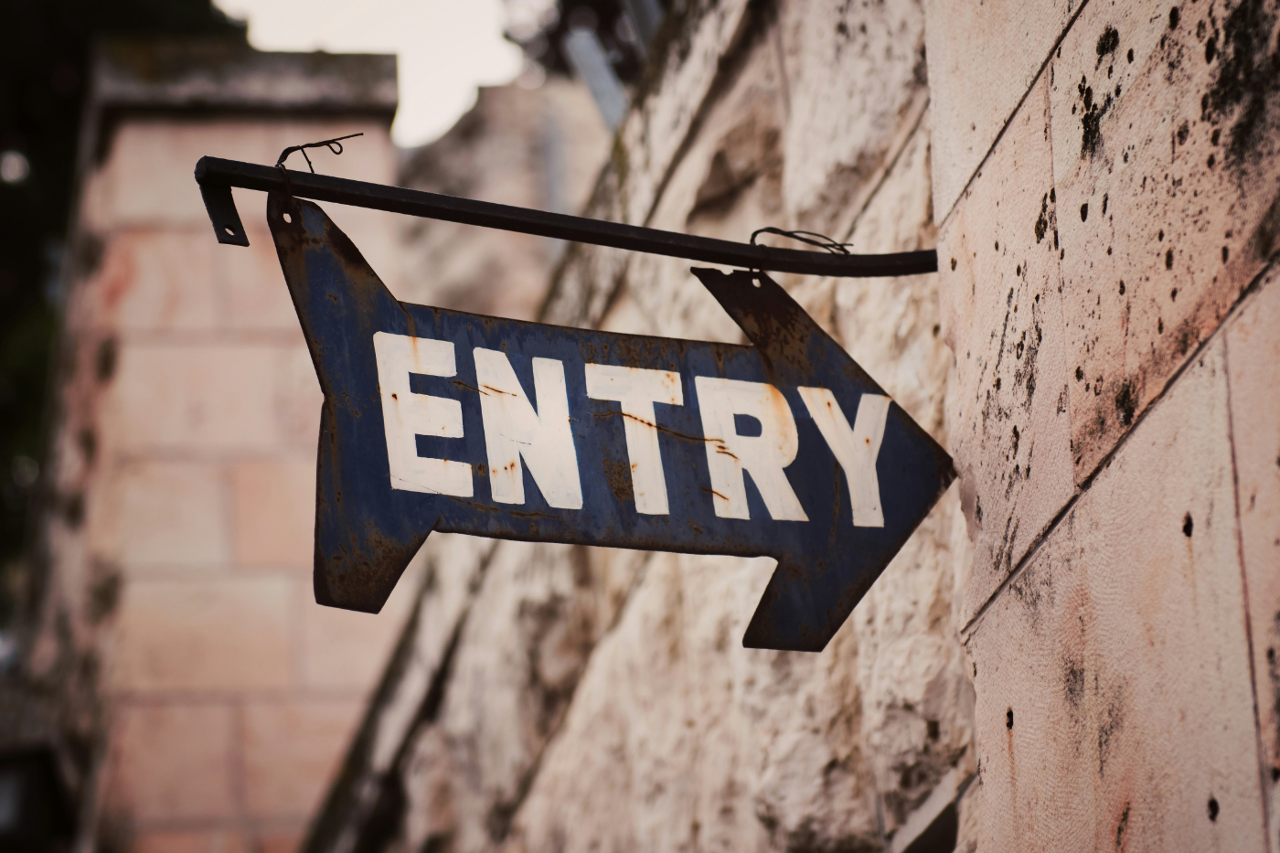 A black, rusty arrow shaped sign with white letters saying ENTRY