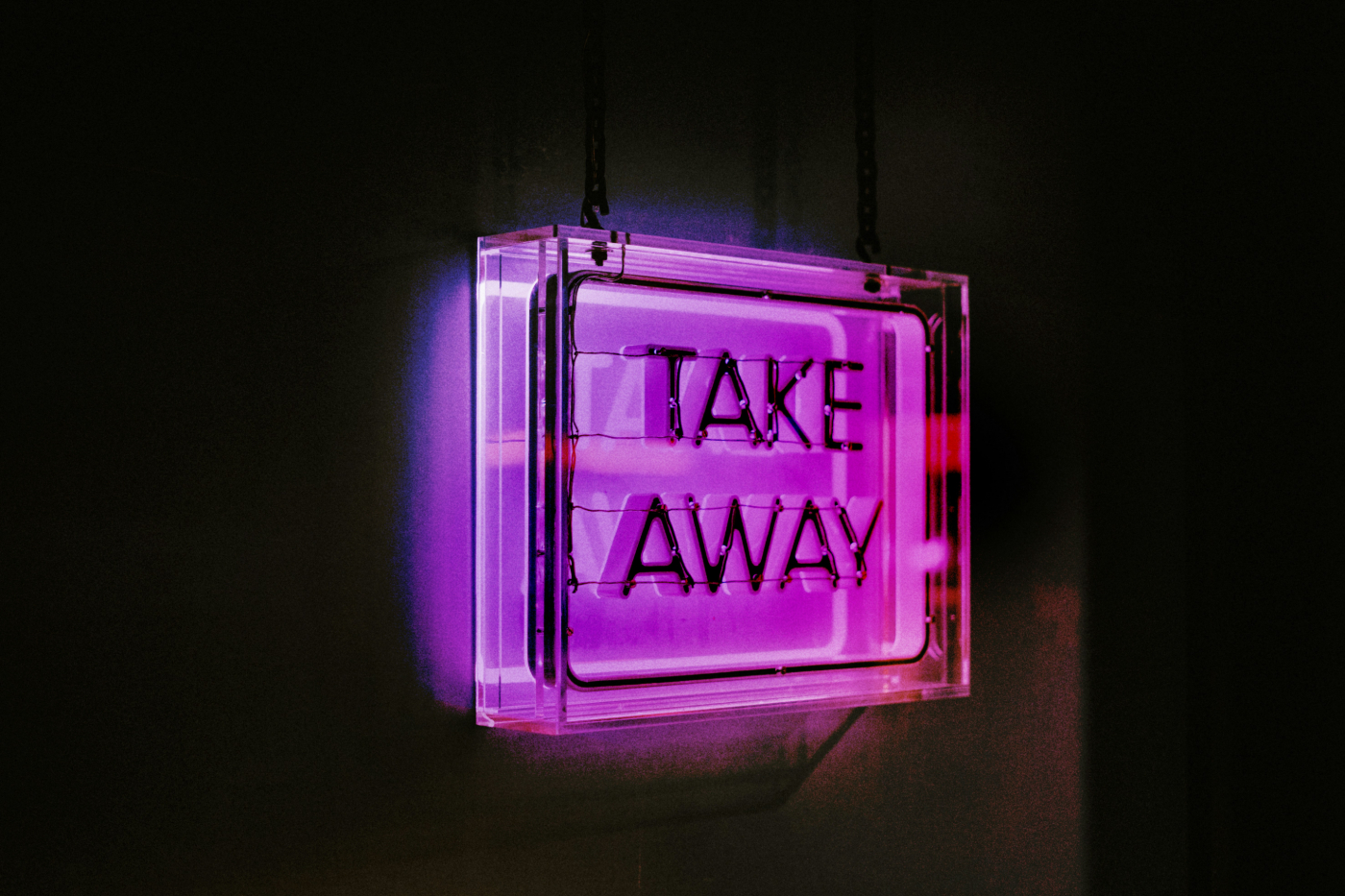 A purple neon sign in a dark room reading Take Away