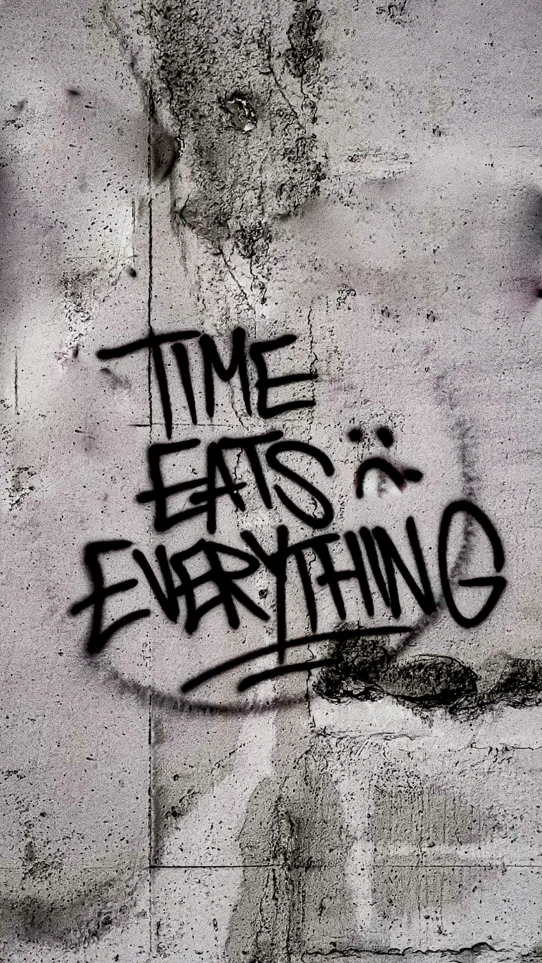 Black graffiti on a gray wall reading: Time Eats Everything