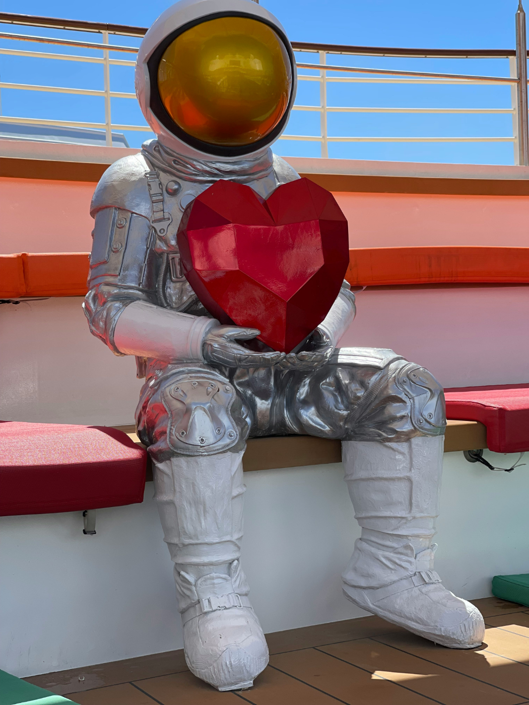 A Statue of an Astronaut sitting on bench holding a heart shaped red object