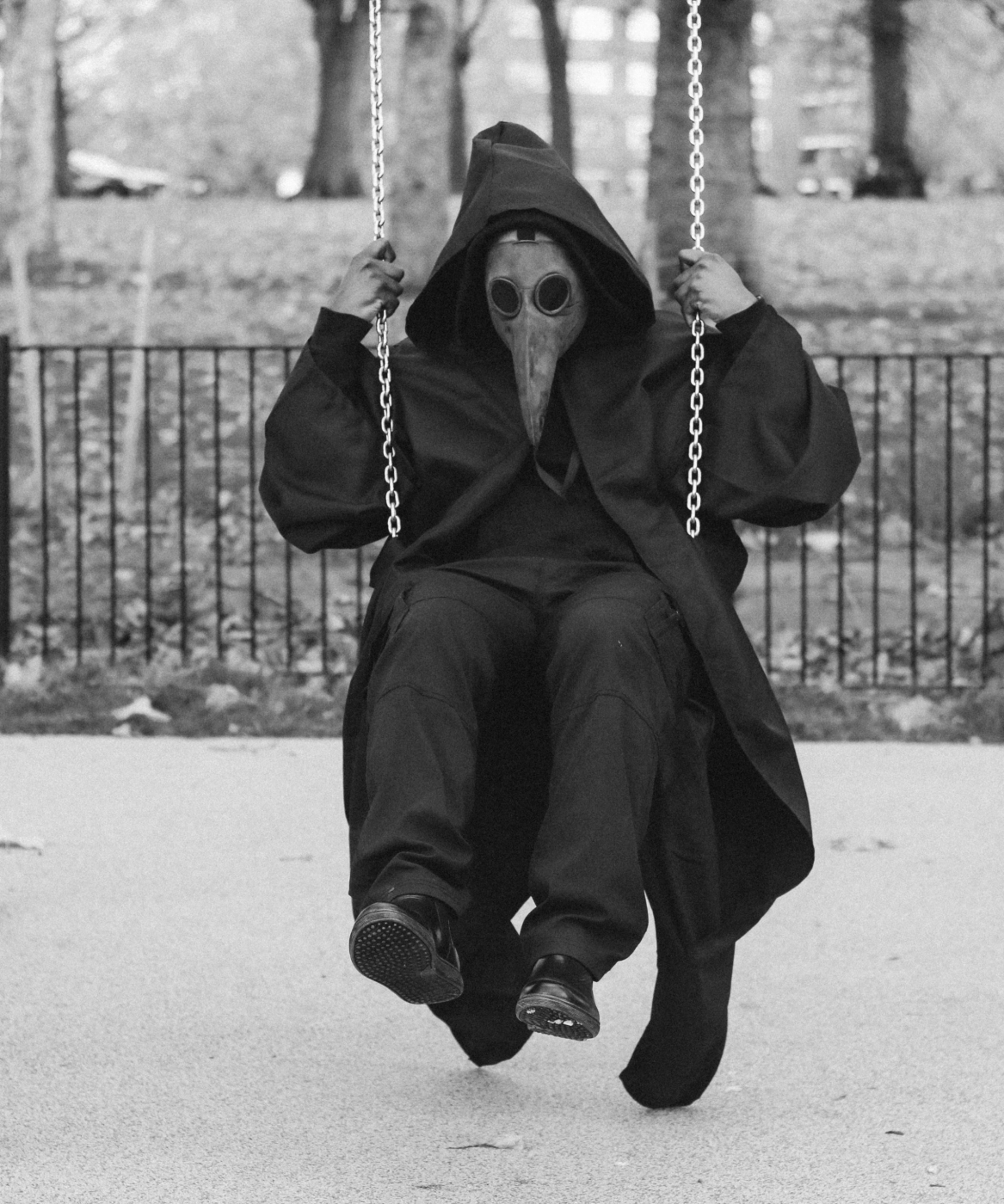 A personal all in black wearing a a plague mask on a swing