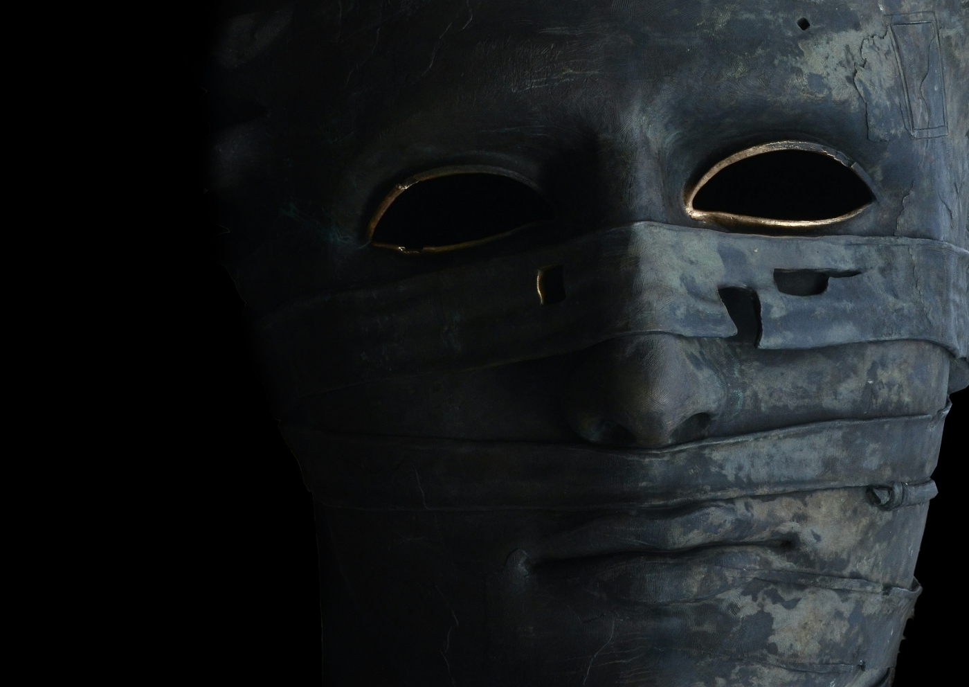 A grey mummy mask with gold painted around the eye holes