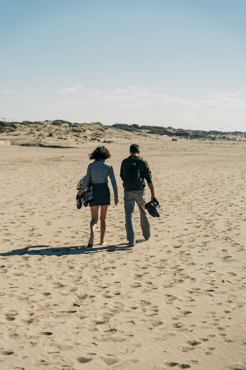 A man and a woman walking barefoot on a beach