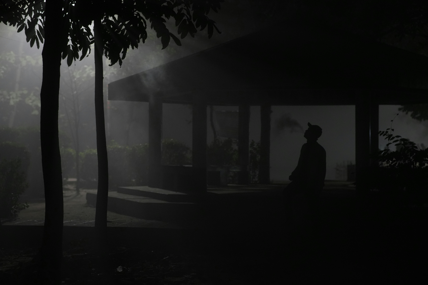 A man in a baseball hat standing in the dark shadows