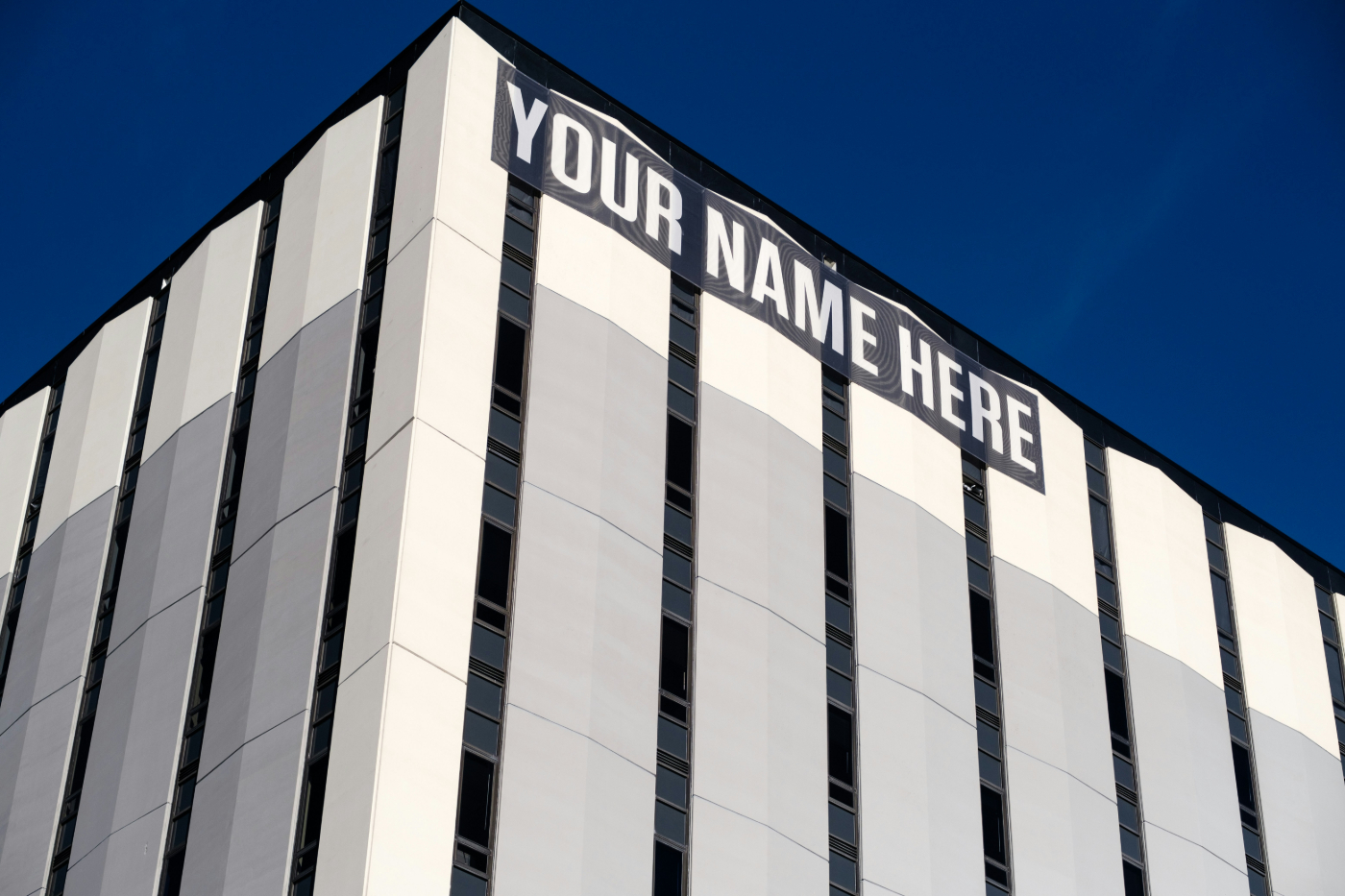 The side of a gray and white building with a banner at the top reading: YOUR NAME HERE