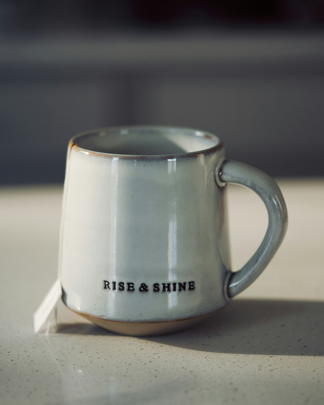 A gray coffee mug with rise & shine on it