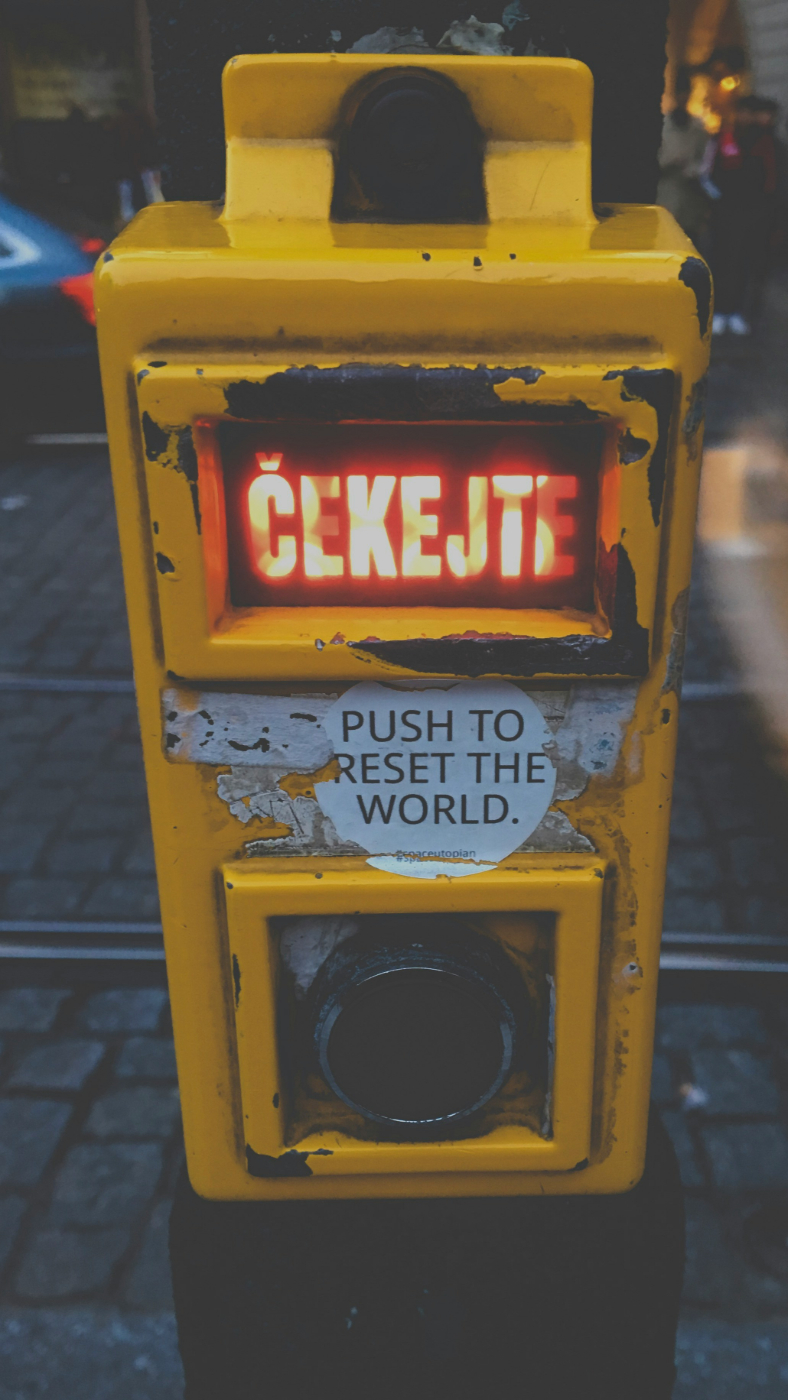 A yellow box with the word wait in Czech in red and a round sticker that reads; Push to reset the world