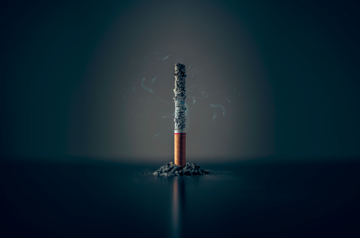 A cigarette. completely ash, standing on it's filtered end which is surrounded by ash
